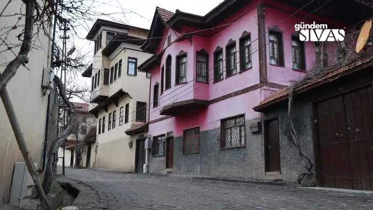 Dar taş döşeli sokakta, farklı renklerde geleneksel konaklar ve bitişik evler sıralanıyor.
