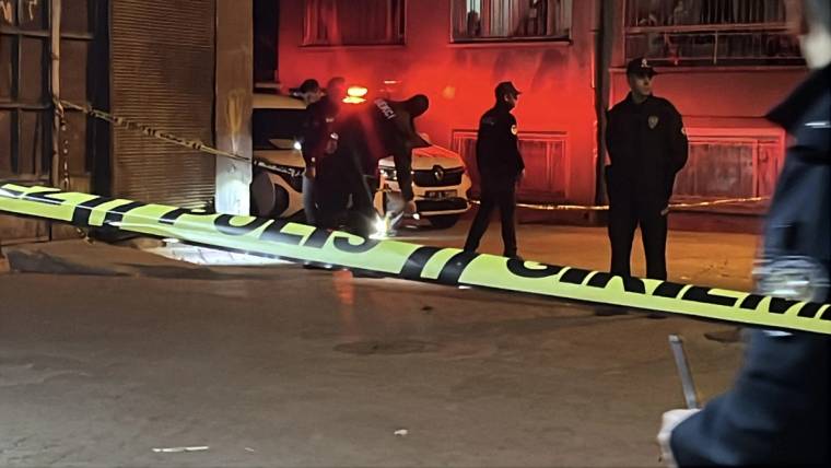 Gece vakti polis şeridiyle çevrilen sokakta, üniformalı görevliler ve bir ambulans görülüyor.