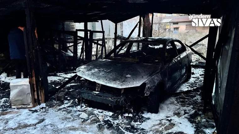Yanmış bir otomobil, is ve külle kaplı zeminde, ahşap bir yapının içinde duruyor.
