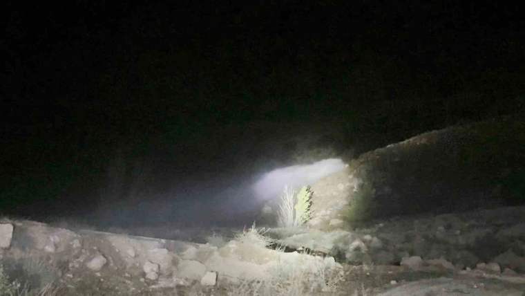 Gece karanlığında taşlı bir kanaldan taşan su, el feneri ışığında ilerliyor.
