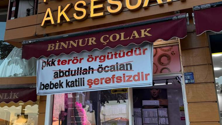 Takı ve aksesuar dükkânının cephesinde “Binnur Çolak” yazılı tente ve sloganlı bir pankart görülüyor.