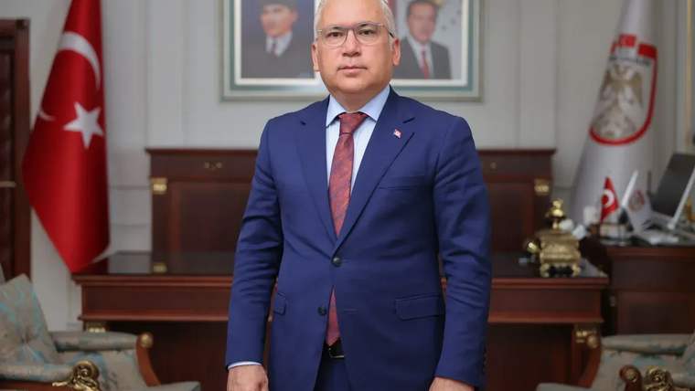 Sivas Valisi, mavi takım elbise giymiş, ofisinde duruyor. Arkada Türk bayrağı ve iki çerçeveli portre var.