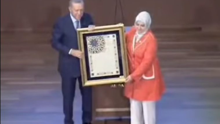 Bir kadın, elinde bir tablo tutarak yanında duran bir erkeğe sunuyor.