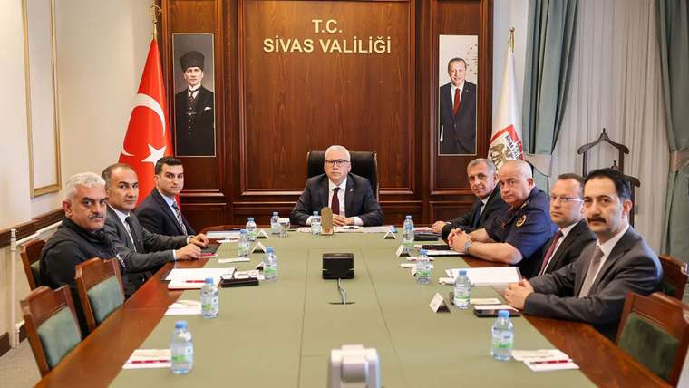Sivas Valiliği'nde bir toplantı, masada yedi kişi oturuyor, arka planda Türk bayrağı ve valilik tabelası var.