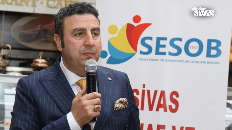 Mikrofon tutan takım elbiseli bir kişi, arkasında Sivas ESOB logosu ve yazıları bulunan panonun önünde.