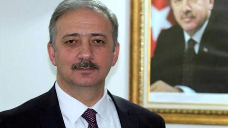 Kadem Mete, resmi bir ortamda, arkasında bir portre ile poz veriyor.
