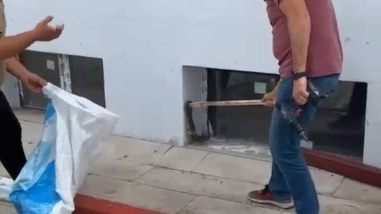 Bir kişi, elindeki uzun çubuğu açık pencere önünde tutarken yanında açık bir çuval görülüyor.