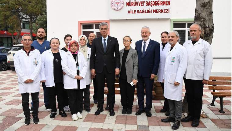 Üzerinde Mürüvvet Başdeğirmen Aile Sağlığı Merkezi yazan binanın önünde sağlık çalışanları ve üç kişi duruyor.