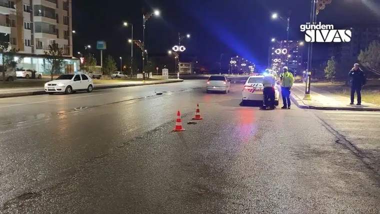 Gece aydınlatılan yolda trafik konileri, ışıkları açık bir araç ve yanında duran iki kişi görülüyor.
