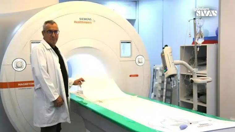 Beyaz önlük giymiş bir doktor, manyetik rezonans görüntüleme cihazının yanında duruyor.