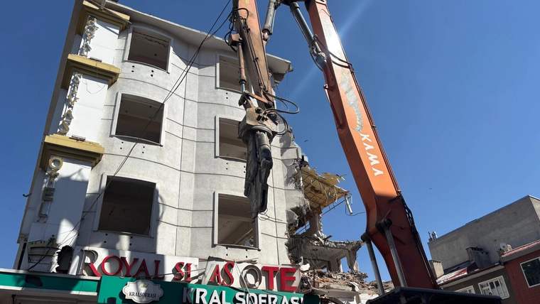 Turuncu bir ekskavatör, alt katında “KRAL SOFRASI” yazan binanın üst bölümünü yıkıyor.