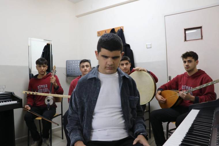 Bir odada, piyanonun önünde oturan bir çocuk ve arkasında üç genç müzisyen, çeşitli enstrümanlar tutuyor.