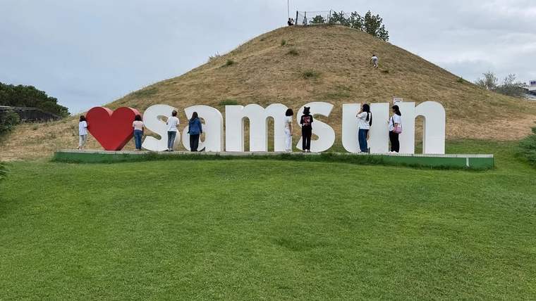 Yeşil bir alanda, "I love samsun" yazılı büyük harflerin önünde birkaç çocuk duruyor.