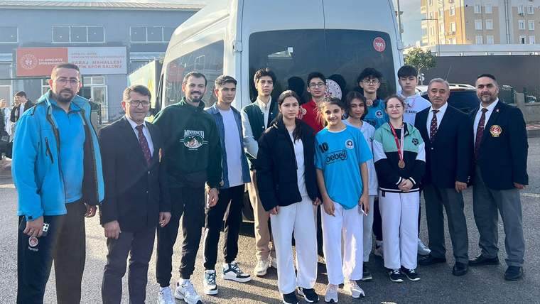 Karete sporcuları, bir otobüsün önünde topluca poz veriyor. Bazıları madalya takmış.