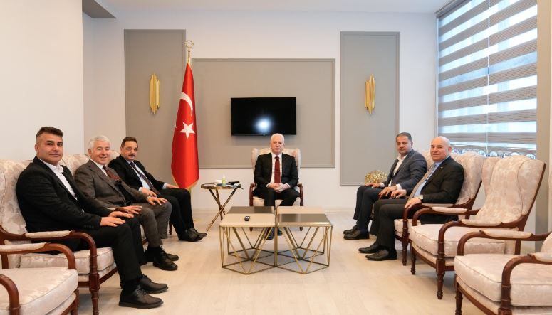 Bir odada Türk bayrağı önünde, ortada oturan bir kişi ve iki yanında sıralanmış yedi kişi görülüyor.