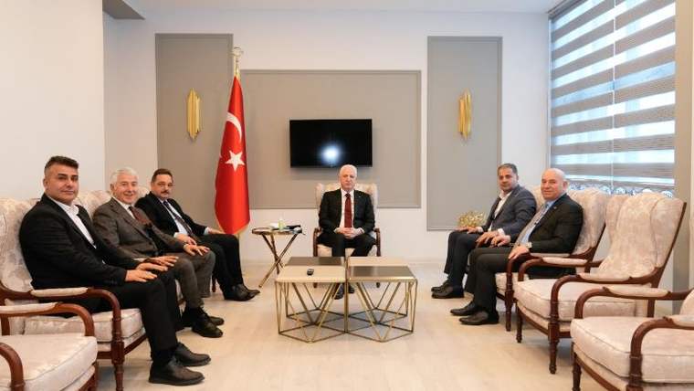 Bir odada Türk bayrağı önünde, ortada oturan bir kişi ve iki yanında sıralanmış yedi kişi görülüyor.