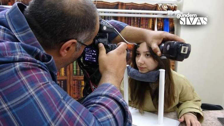 Bir fotoğrafçı, iris fotoğrafı çekerken bir kadının başını destekliyor.