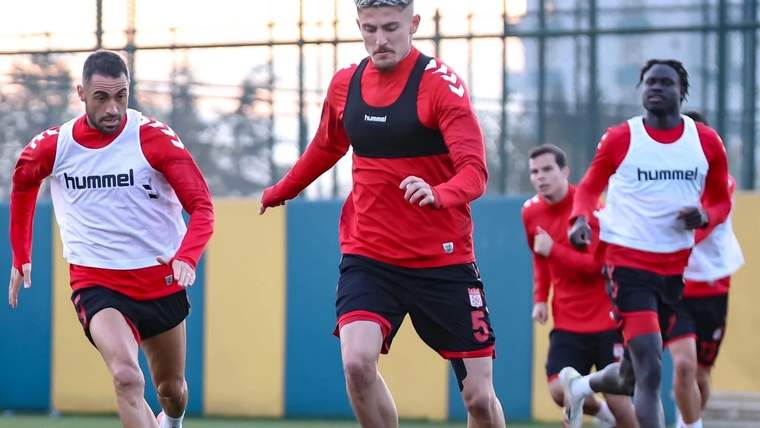 Futbolcular, açık sahada kırmızı-beyaz antrenman formalarıyla top sürerek koşu çalışması yapıyor.