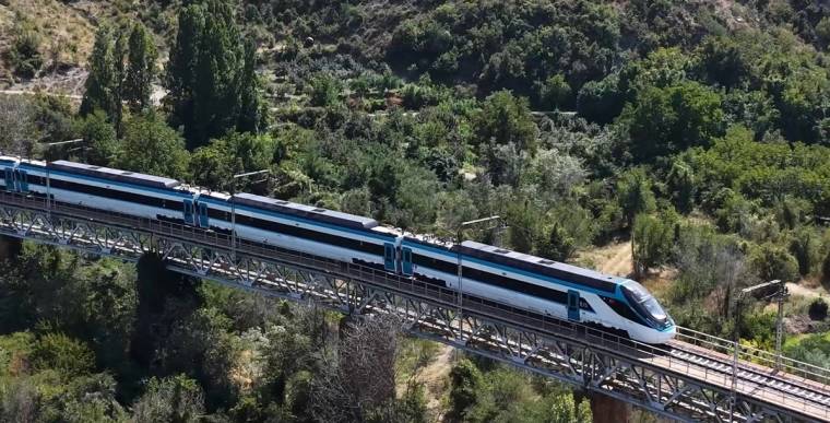 Mavi beyaz renkli hızlı tren, yeşil yamaçlar arasındaki demir köprü üzerinden ilerliyor.