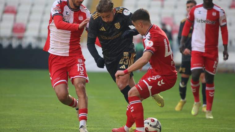 Futbol sahasında kırmızı formalı iki oyuncu, siyah formalı rakipleriyle top mücadelesi yapıyor.