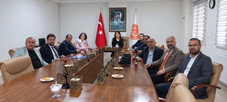 Toplantı masası çevresinde oturan bir grup kişi, Türk bayrağı ve duvardaki portreyle birlikte görülüyor.