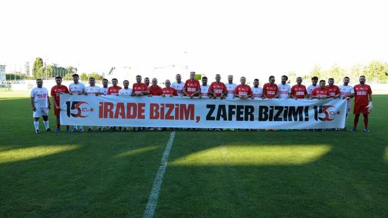 Futbol sahasında yan yana duran oyuncular, üzerinde “İrade bizim, zafer bizim!” yazılı pankartı tutuyor.