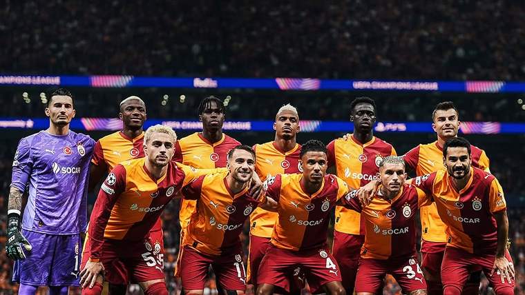 Futbolcular, sahada Galatasaray arması bulunan bir platformun önünde takım halinde poz veriyor.