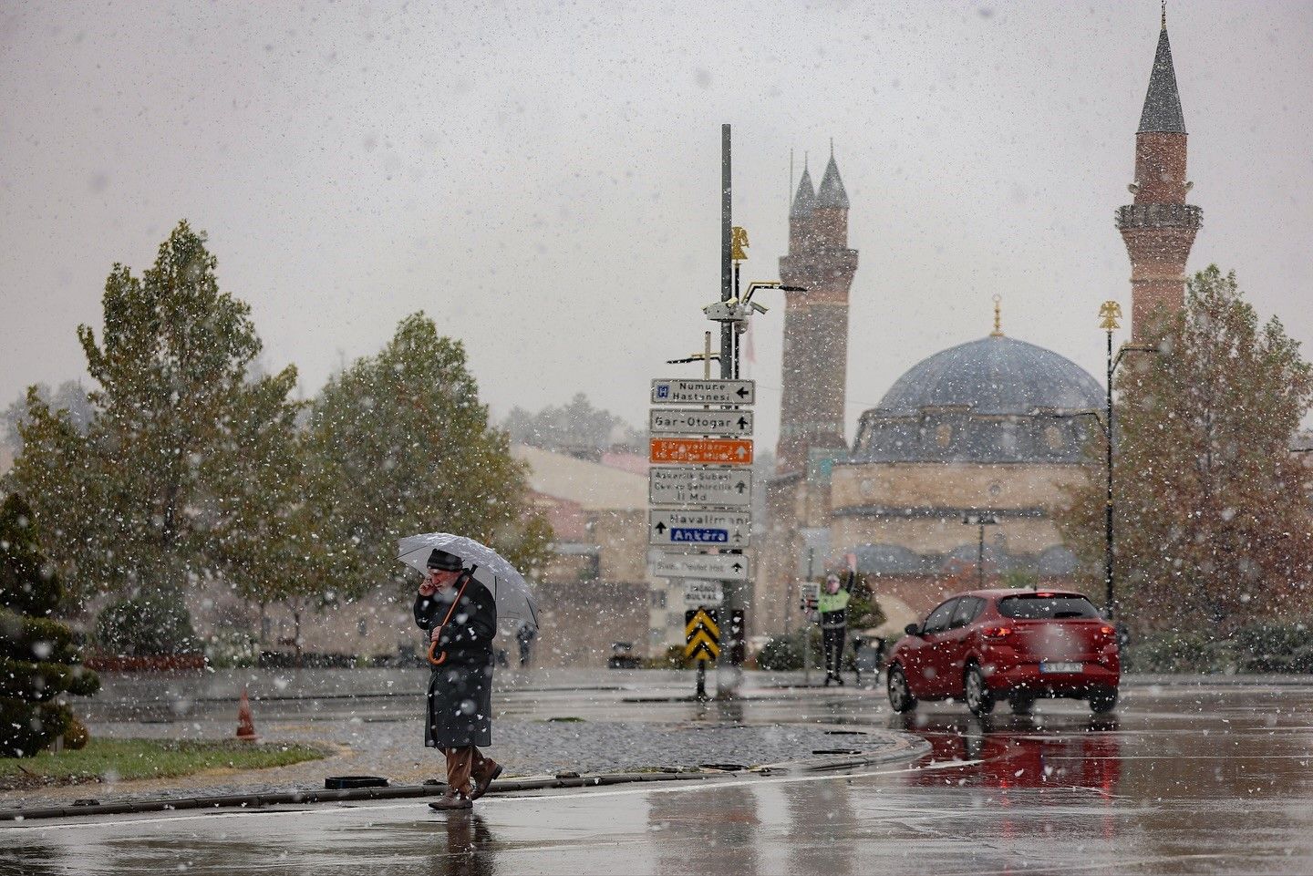 Karla kaplı bir sokakta, şemsiye tutan iki kişi ve arka planda bir cami görünmekte.