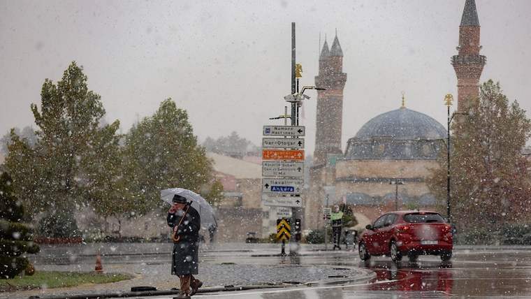 Karla kaplı bir sokakta, şemsiye tutan iki kişi ve arka planda bir cami görünmekte.