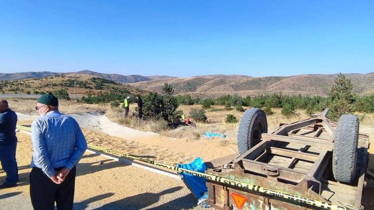Devrilmiş bir traktör, etrafında birkaç kişi ve dağlık bir manzara görünmekte.