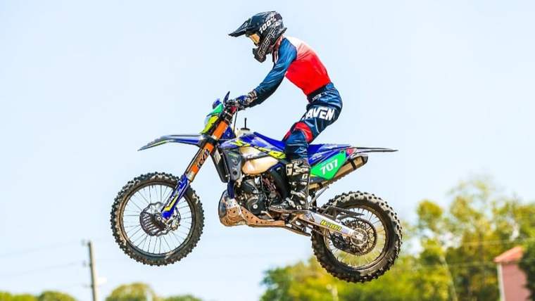 Hava da zıplayan bir motocross motosikleti üzerinde bir sporcu, yarış kıyafetleriyle havada.