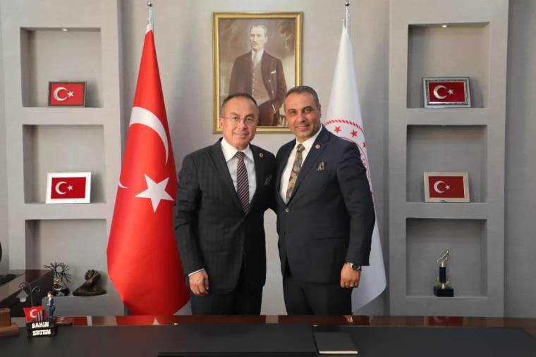 İki kişi, arka planda Türk bayrağı ve Atatürk portresi ile birlikte gülümsüyor.