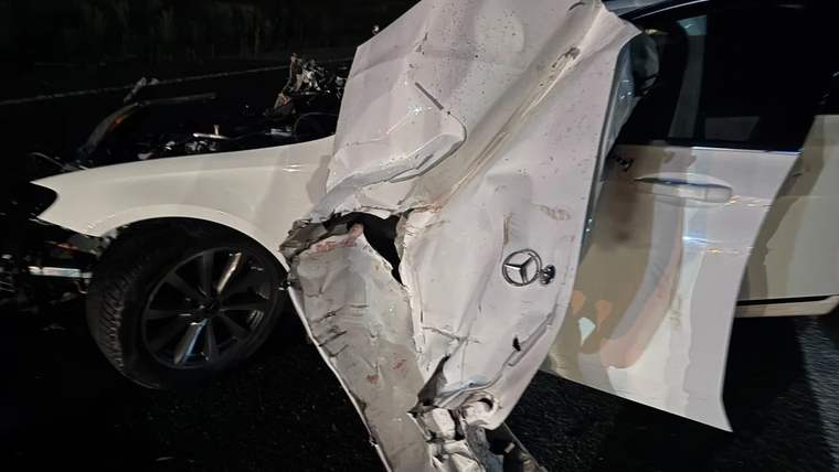 Gece karanlığında, ön ve yan bölümü ağır hasar alan beyaz otomobil yol üzerinde duruyor.