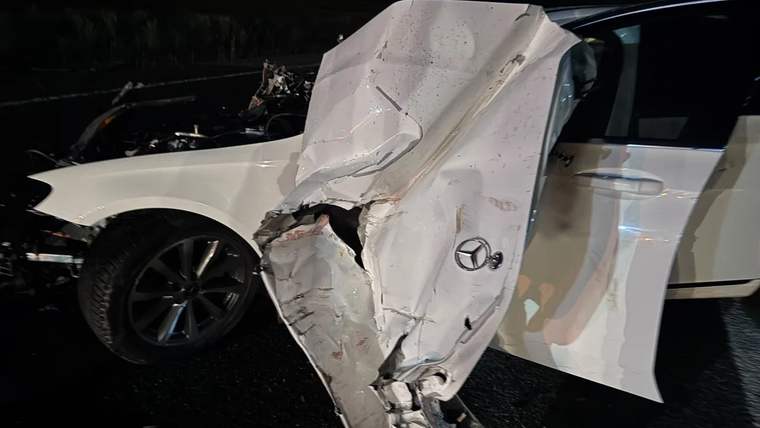Gece karanlığında, ön ve yan bölümü ağır hasar alan beyaz otomobil yol üzerinde duruyor.