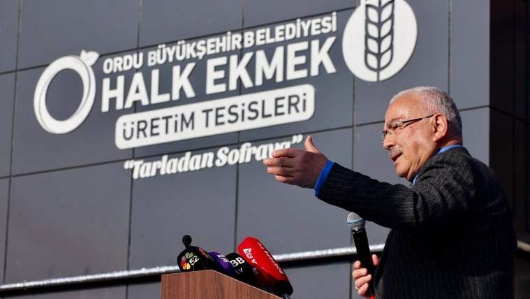 Bir kişi, üzerinde Ordu Büyükşehir Belediyesi Halk Ekmek Üretim Tesisleri yazan bina önünde konuşuyor.