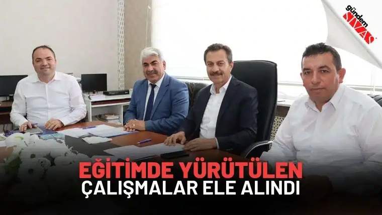Dört kişi, masanın etrafında oturmuş, belgelerle çalışıyorlar.