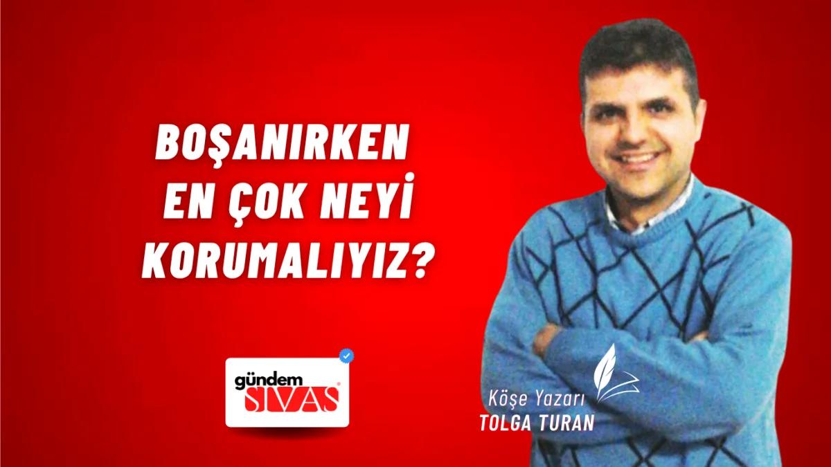 Mavi kazak giymiş bir erkek, kırmızı arka planda gülümsüyor.