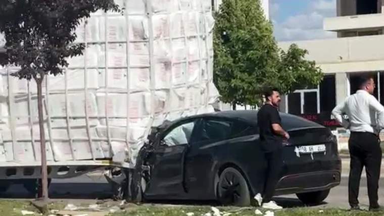 Beyaz yük aracının yanında duran siyah otomobilin ön kısmı ağır hasarlı; yakınında iki kişi var.