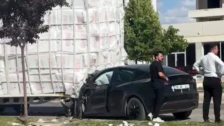Beyaz yük aracının yanında duran siyah otomobilin ön kısmı ağır hasarlı; yakınında iki kişi var.