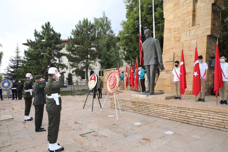 Askeri üniformalı kişiler, Türk bayrakları ve çelenklerin bulunduğu anıt önünde tören düzenliyor.