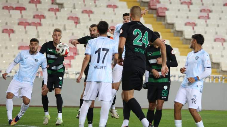 Futbol sahasında siyah ve beyaz formalı oyuncular, havadaki topa doğru hareketleniyor.