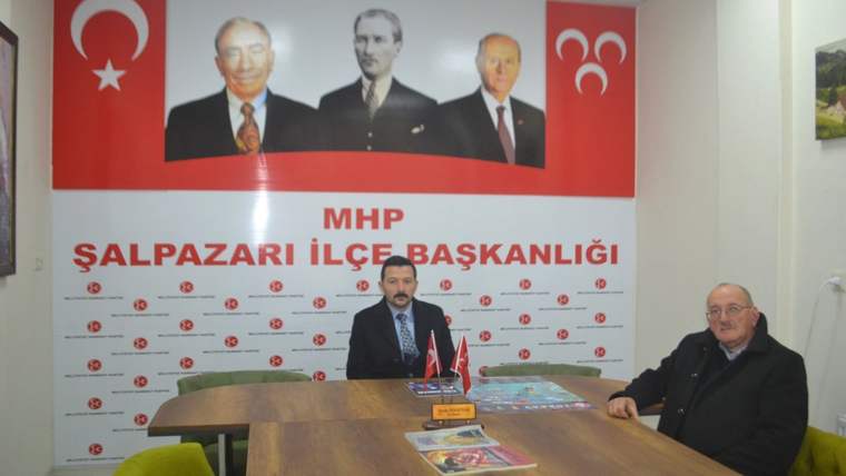 MHP Şalpazarı İlçe Başkanlığı'nda, iki kişi masada oturuyor; arka planda MHP liderlerinin portreleri var.