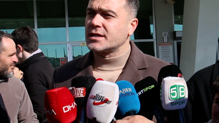 Bir kişi, bina girişinde DHA, Haber Global ve 58 Spor logolu mikrofonlara konuşuyor.