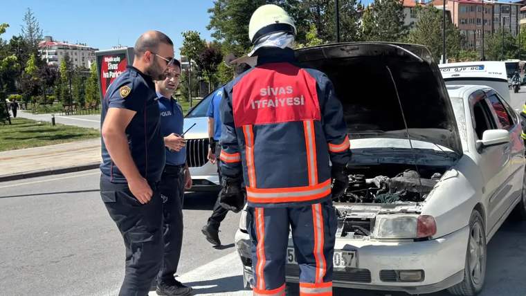 Kaputu açık bir otomobilin önünde, itfaiye kıyafeti giymiş bir kişi ve iki polis memuru duruyor.