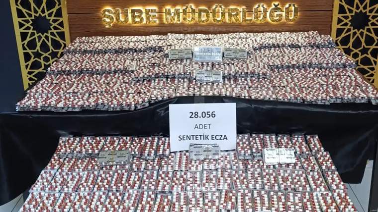 Üzerinde '28.056 adet sentetik ecza' yazılı bir tabela, yanına dizilmiş uyuşturucu hapların bulunduğu masa.