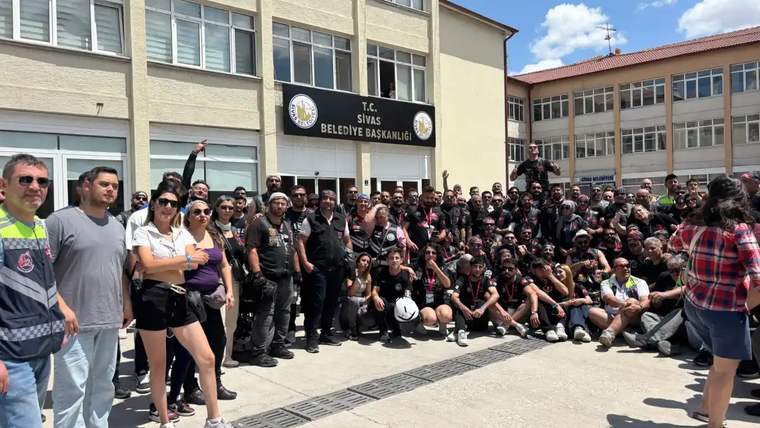 Sivas Belediyesi binası önünde, motosiklet kıyafetleri giyen kalabalık bir grup toplu halde duruyor.