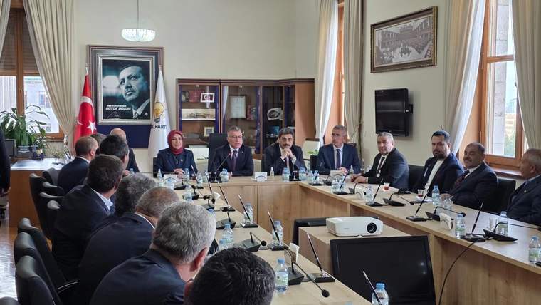 Toplantı salonunda uzun masa etrafında oturan kişiler, Türk bayrağı ve duvardaki portreyle görülüyor.