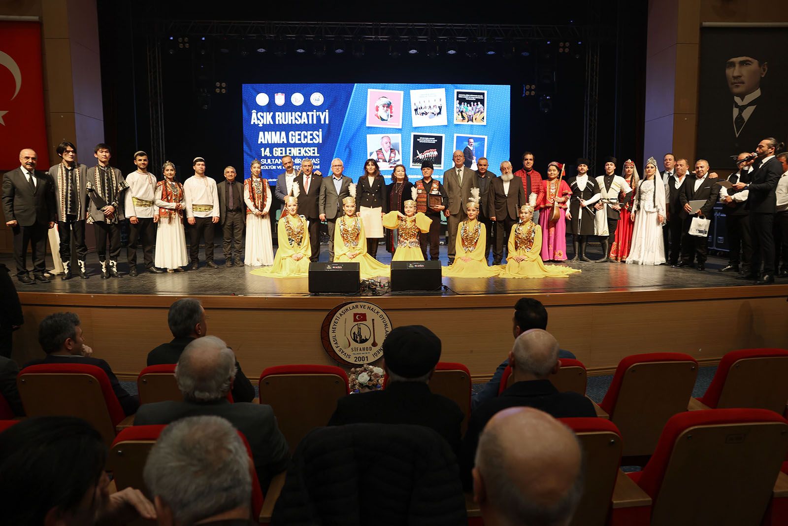 Sahne üzerinde çeşitli kostümler giymiş insanlar, anma etkinliğinde bir araya gelmiş.