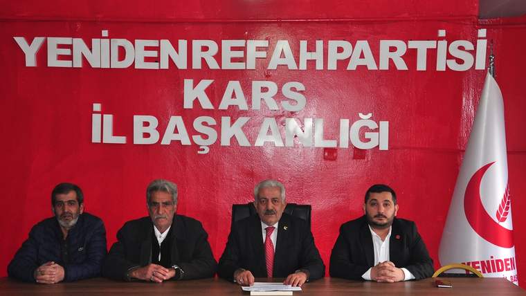 Kırmızı duvar önünde, üzerinde Kars İl Başkanlığı yazan masada dört erkek yan yana oturuyor.