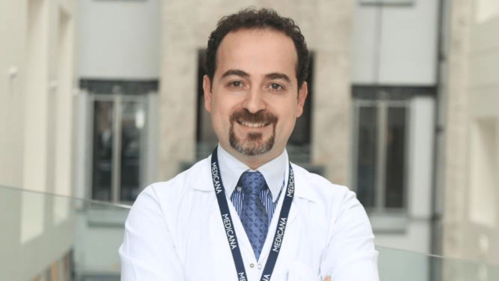 Beyaz önlük giymiş, kravat takan bir doktor gülümsüyor.
